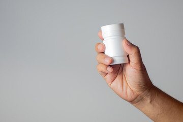 The man's hand held a medicine bottle containing antibiotics against a white background. - obrazy, fototapety, plakaty