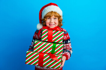 Photo of good mood cute little boy dressed ugly pullover x-mas hat getting presents isolated blue color background
