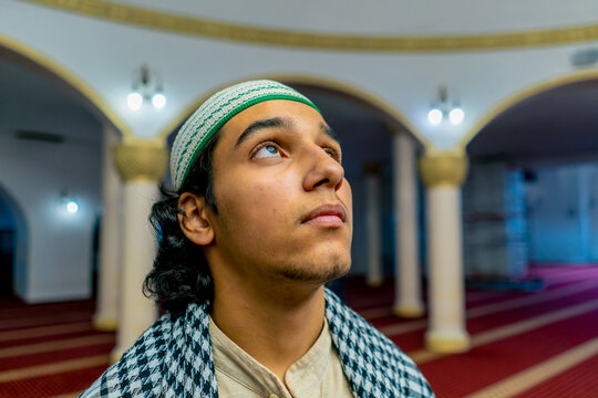 Close-up shot of a Muslim man's face standing on a carpet in the middle of a prayer hall at mosque with his head raised up
