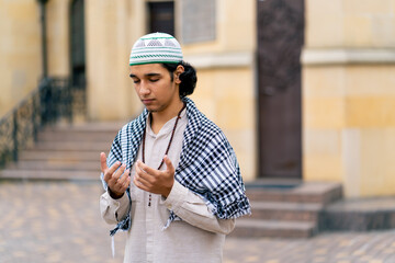 A guy of Arab appearance in national clothes with rosary around his neck prays in the courtyard of...