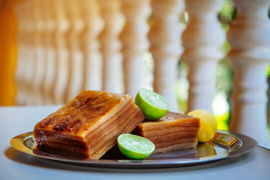 Bebinka is a traditional Goan layer cake from coconut milk and nutmeg. Dessert of 10 layers with limes on an iron plate on a light background and sunlight close up.