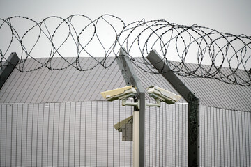Barbed wire and big metal fence with surveillance cameras. Border, prison, criminals and war concept. - obrazy, fototapety, plakaty