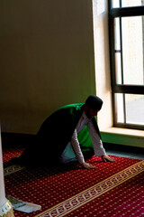 A Muslim believer prays in the twilight by a window in a mosque kneels down puts his forehead on carpet and turns to Allah