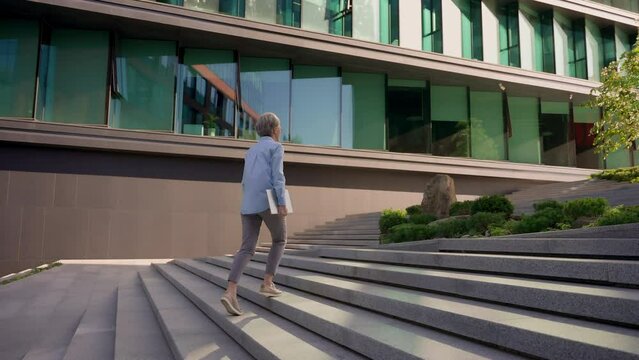 Back view businesswoman middle-aged lady manager CEO entrepreneur leader professional lawyer unrecognizable woman walking outdoors to office building city business center walk up stairs climbing steps