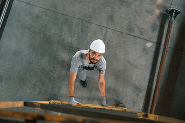 Going up on the ladder, top view. Young factory worker in grey uniform