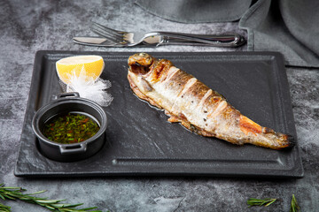 River trout baked in josper with sauce and lemon on a dark background