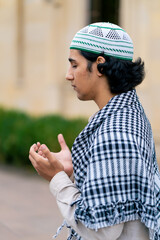 A guy of Arab appearance in national clothes with rosary around his neck prays in the courtyard of the mosque