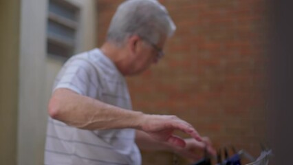 Authentic Daily Routine of a Senior Man Hanging Clothes to Dry in Backyard. Candid Household Activity Depicting Active Lifestyle in Old Age