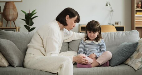 Mother lovingly strokes saddened daughter while engaged in a heartfelt conversation, sitting together on the couch. Their interaction reflects a nurturing and empathetic moment of connection.