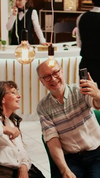 Vertical Video Elderly people taking photos in lobby, recording all activities on retirement vacation abroad. Old husband and wife take pictures on smartphone, making memories for family members.