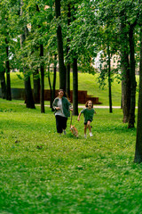 Fototapeta premium family young mother walking in the park with her daughter and red dog running forward on the grass happy childhood love for animals