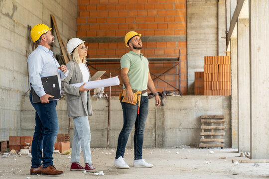 A female architect and construction managers work together on-site, discussing blueprints and coordinating to bring their project to life.	