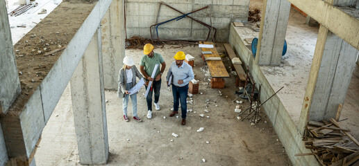 A female architect and construction manager work together on-site, discussing blueprints and coordinating to bring their project to life. Image taken from above.