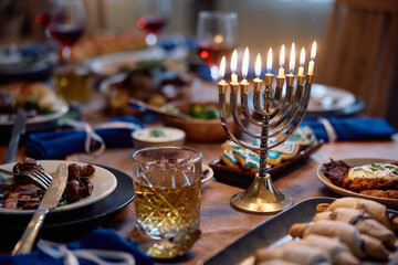 Lit candles in menorah on dining table during Hanukkah meal at home.