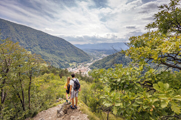 Young, embraced couple enjoying the fantastic mountain and valley panorama, taking a break on a viewpoint after a hike on a sunny summer day