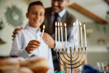 Close up of boy lighting candles in menorah with his father during Hanukkah celebration.