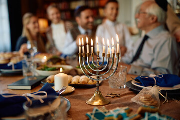 Lit candles in menorah with Jewish multigeneration family gathered for Hanukkah celebration. - obrazy, fototapety, plakaty