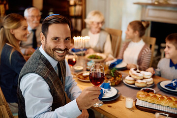 Happy Jewish man toasting during family meal on Hanukkah at looking at camera.