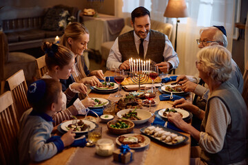 Happy multigeneration Jewish family eating dinner at dining table on Hanukkah.