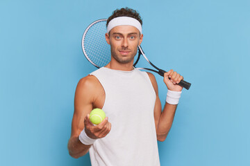 Tennis player in white t-shirt puts tennis racket on his shoulder, holds out tennis ball in one hand, sports life concept, copy space
