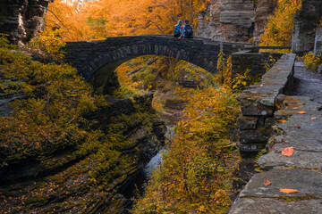 Senior couple stands on stone bridge over a river in deep gorge surrounded by autumn forest with...