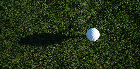Overhead view of a golf ball projecting an overhang on the grass of a golf course. Copy space on the left. Concept backgrounds and textures.