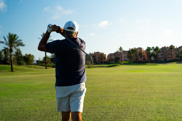 Elderly golfer taking a swing on the course of a golf club. Copy space on the right