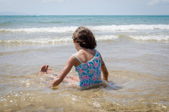 Brunette Girl with Blue Swimsuit Enjoying Shallow Sea at Sandy Beach at Summer. Tranquil Coastal Scene in Greece. Horizon and Sky in Background.