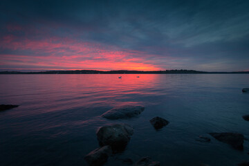 Landscape sunset with pink horizon and dark grey clouds over water with rocks in Stockholm.. Original public domain image from Wikimedia Commons