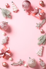 Christmas frame of baubles, fir branches, gift boxes on pink table. Xmas background. Flat lay, top view.