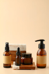 Set of amber glass cosmetic bottles and jar of moisturizer cream on stone and wood podium. Natural beauty products display.