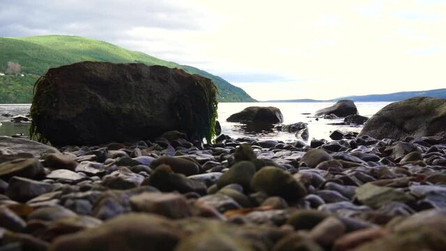 Wet pebbles and a moss-covered rock on the shore of Loch Ness. Low angle view.