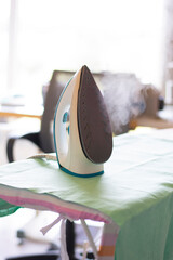 Steam coming from an modern iron standing on an ironing board close-up, vertical photo on a blurred background. Composition of housework, ironing and women's labor