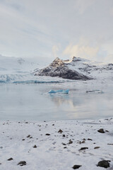 A serene wintry scene with a vast lake and snow-capped mountains at the sunset. Icebergs float in the lake under a clear blue sky.