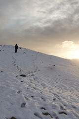 Sunset over a snowy landscape with a person ascending a hill