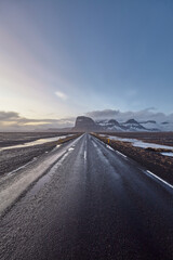 Scenic road winding through Iceland's desolate beauty, with snow-capped mountains, a setting sun,...