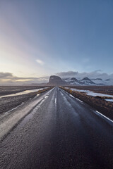 Scenic road winding through Iceland's desolate beauty, with snow-capped mountains, a setting sun, and a sense of tranquility.