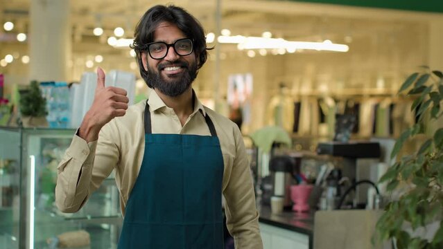 Coffee shop worker show like agree recommend gesture approve hand symbol successful happy smiling cafe waiter guy Indian Arabian male cafeteria working showing thumb up barista man small business