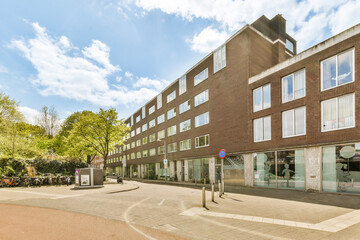 an empty street in front of a large brick building with many windows on each side and cars parked...