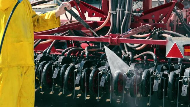Washing of large-sized agricultural machinery. Cleaning the seeder after work in the field. A worker washes an agricultural machine with water under pressure.