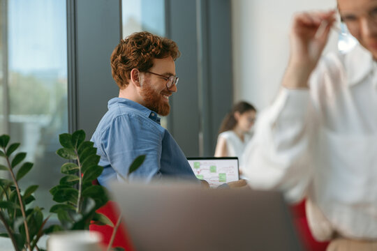 Smiling male sales manager in eyeglasses working on laptop sitting in office during working day