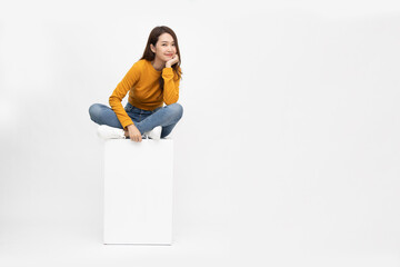 Smiling young Asian woman sitting on white box isolated on white background