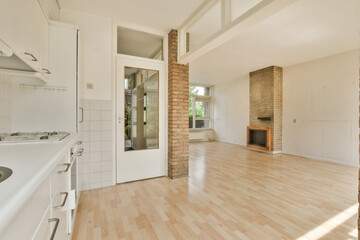 an empty living room with wood flooring and white appliances on the stove in the kitchen is visible to the right