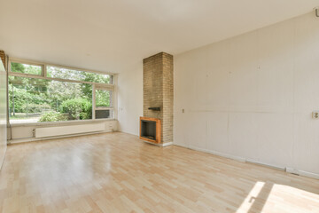 an empty living room with wood flooring and large windows looking out onto the backyard garden in the back wall