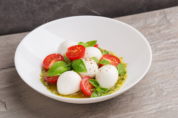 Caprese salad with tomato, mozzarella, basil, pesto sauce on white plate on dark table. Italian cuisine. Isometric food.