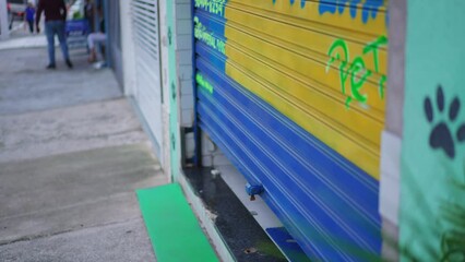 Man closing storefront garage in city sidewalk. Person slides storefront in street