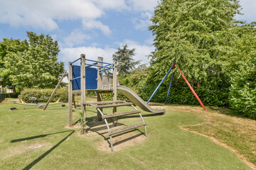 a playground with swings, slides and slides in the grass area next to some trees on a sunny day