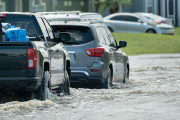 Hurricahe rainfall flooded Florida road with evacuating cars and surrounded with water houses in...