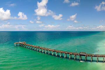 Venice fishing pier in Florida on sunny summer day. Bright seascape with surf waves crashing on sandy beach