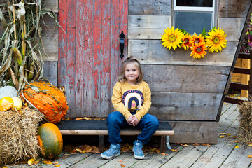
Adorable smiling little blond girl sitting on the steps of a hut decorated with pumpkins for...